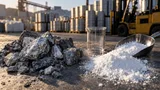Overhead shot of raw gray lithium ore chunks and loose white salt-like lithium carbonate powder arranged in separate neat piles on a concrete industrial surface, with a stainless steel scoop and a small empty glass beaker resting beside the