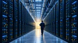 Wide interior view of a large, modern data center with long rows of illuminated server racks and a lone technician walking through the aisle, evoking the scale of cloud infrastructure growth.
