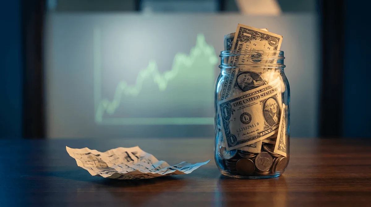 A close-up shot of a clear glass jar overflowing with crisp dollar bills and coins, positioned next to a wilting or deflated paper earnings report, visually contrasting real cash versus misleading numbers.